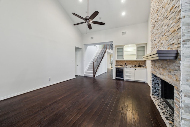 unfurnished living room with dark wood-type flooring, a fireplace, high vaulted ceiling, ceiling fan, and beverage cooler