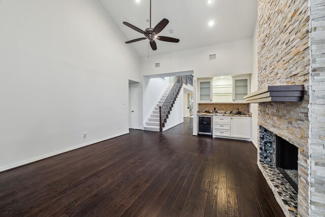 unfurnished living room with ceiling fan, high vaulted ceiling, dark hardwood / wood-style floors, wine cooler, and a stone fireplace