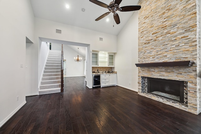 unfurnished living room with high vaulted ceiling, beverage cooler, hardwood / wood-style flooring, a fireplace, and ceiling fan with notable chandelier