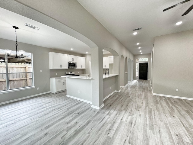 kitchen with kitchen peninsula, stainless steel appliances, pendant lighting, white cabinets, and light hardwood / wood-style floors