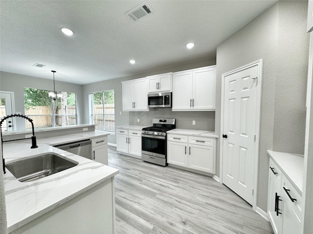 kitchen featuring tasteful backsplash, stainless steel appliances, sink, white cabinets, and hanging light fixtures