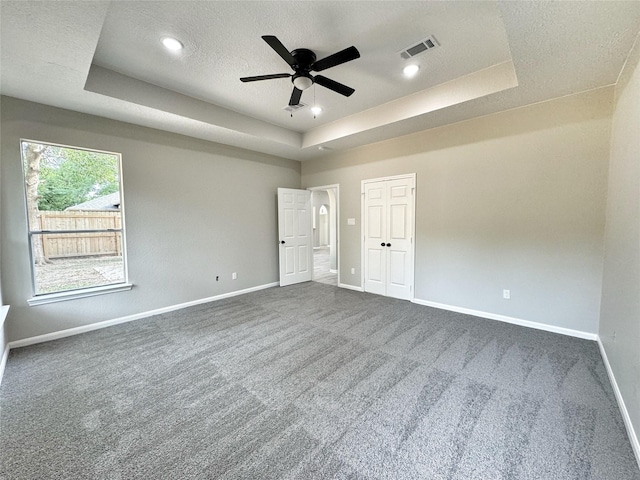 unfurnished bedroom featuring a textured ceiling, a tray ceiling, ceiling fan, dark colored carpet, and a closet