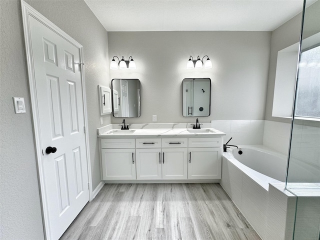 bathroom featuring hardwood / wood-style floors, vanity, tiled bath, and a textured ceiling