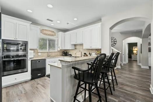 kitchen with white cabinets, oven, decorative backsplash, and black dishwasher