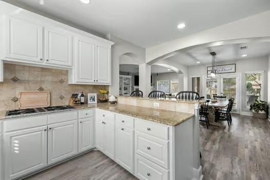 kitchen featuring white cabinets, light wood-type flooring, decorative light fixtures, kitchen peninsula, and stainless steel gas cooktop