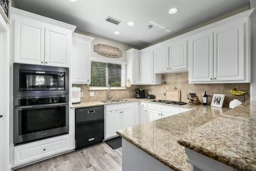 kitchen featuring black appliances, light stone countertops, white cabinetry, and sink