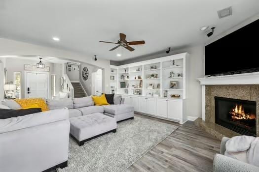 living room featuring a high end fireplace, light wood-type flooring, and ceiling fan