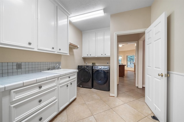 clothes washing area with sink, cabinets, independent washer and dryer, a textured ceiling, and light tile patterned flooring