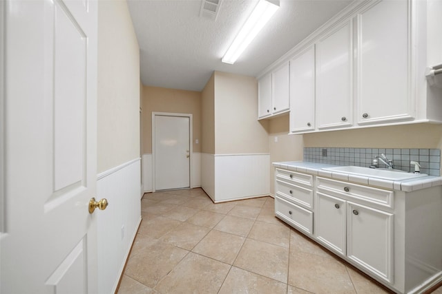 laundry area with a textured ceiling, light tile patterned flooring, and sink