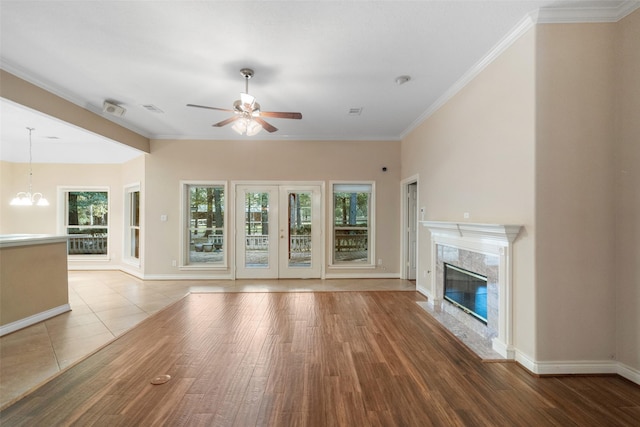 unfurnished living room with ceiling fan with notable chandelier, hardwood / wood-style flooring, crown molding, and a premium fireplace