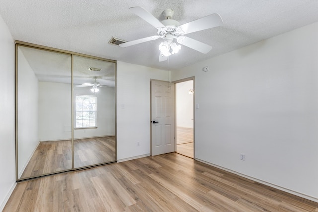 unfurnished bedroom featuring ceiling fan, a closet, a textured ceiling, and light wood-type flooring