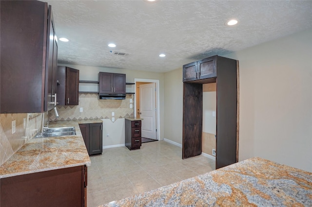 kitchen with a textured ceiling, dark brown cabinetry, sink, and tasteful backsplash