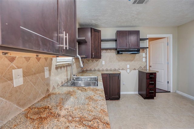 kitchen featuring dark brown cabinets, a textured ceiling, light stone counters, and sink