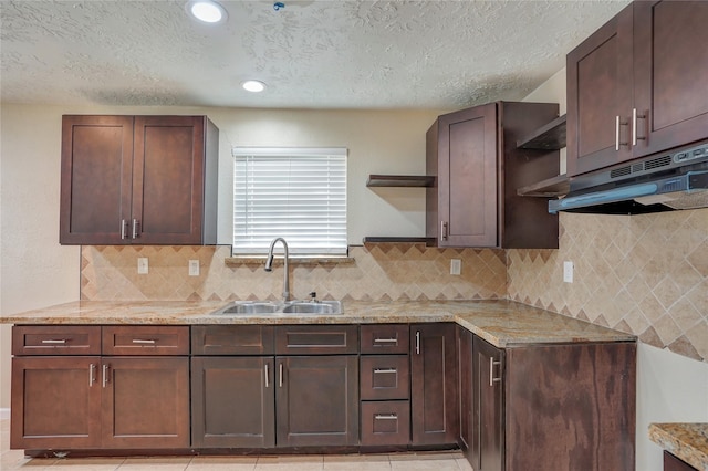 kitchen with decorative backsplash, light stone counters, a textured ceiling, dark brown cabinetry, and sink