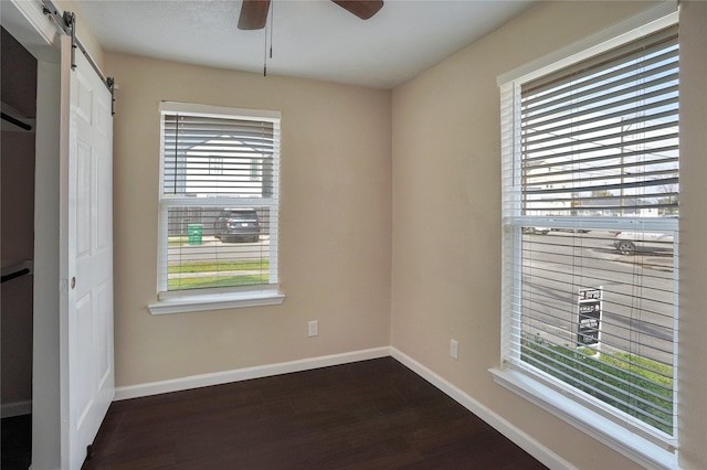 unfurnished bedroom with a barn door, a closet, ceiling fan, and dark wood-type flooring