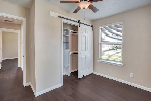 unfurnished bedroom featuring a barn door, ceiling fan, a closet, and multiple windows