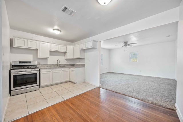 kitchen with white cabinets, sink, light hardwood / wood-style flooring, ceiling fan, and stainless steel range