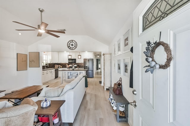 living room with ceiling fan, sink, lofted ceiling, and light wood-type flooring