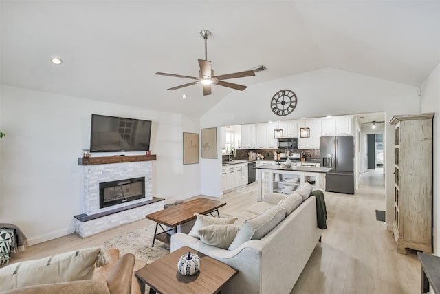 living room with sink, vaulted ceiling, ceiling fan, a fireplace, and light hardwood / wood-style floors