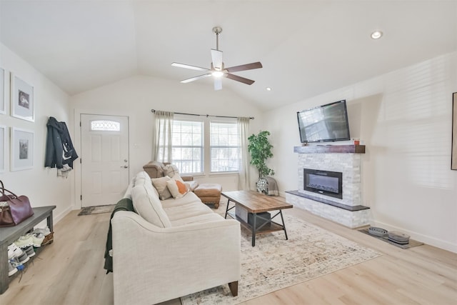 living room with a stone fireplace, ceiling fan, vaulted ceiling, and light wood-type flooring