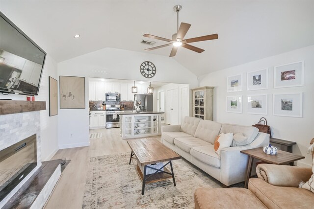 living room featuring light wood-type flooring, ceiling fan, lofted ceiling, and a tiled fireplace