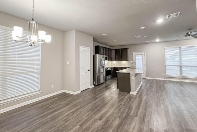 kitchen featuring light stone countertops, ceiling fan with notable chandelier, stainless steel appliances, a kitchen island with sink, and decorative light fixtures