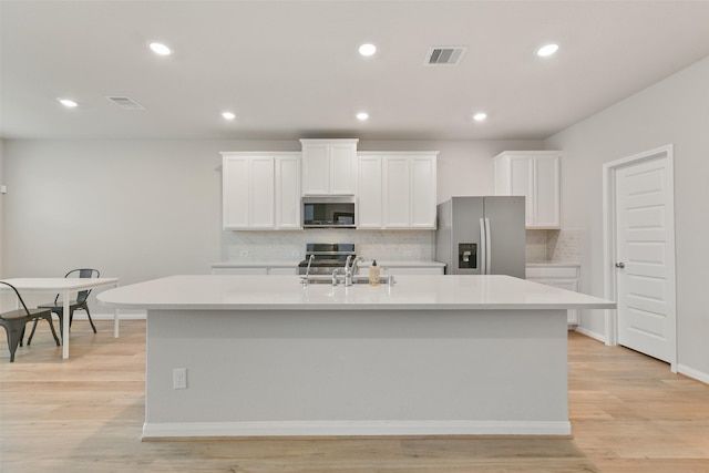 kitchen featuring white cabinets, appliances with stainless steel finishes, a center island with sink, and light hardwood / wood-style floors