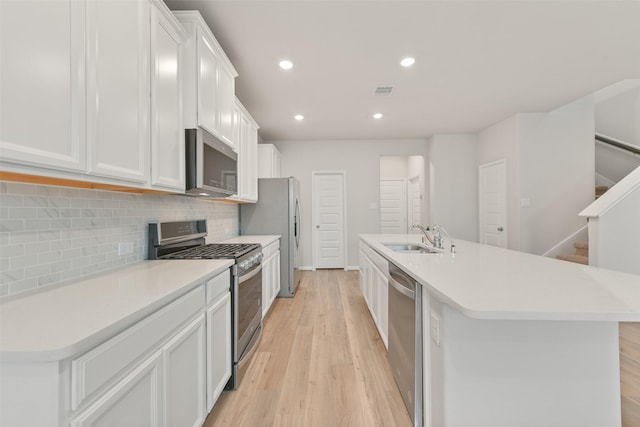 kitchen featuring appliances with stainless steel finishes, tasteful backsplash, sink, a center island with sink, and white cabinets