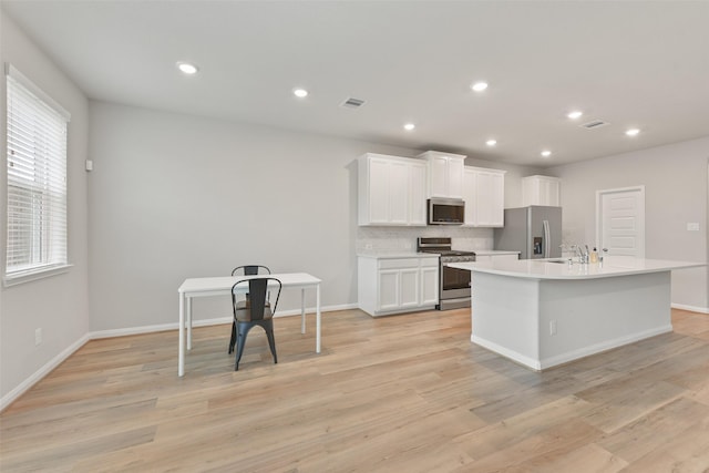 kitchen with a kitchen island with sink, white cabinets, sink, light hardwood / wood-style floors, and stainless steel appliances