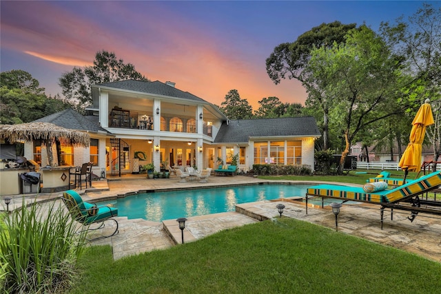 pool at dusk featuring an outdoor bar, a patio, and a yard