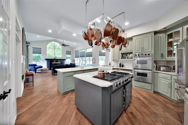 kitchen featuring backsplash, ceiling fan with notable chandelier, stainless steel appliances, a kitchen island, and lofted ceiling