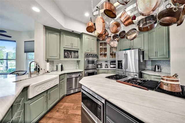 kitchen featuring appliances with stainless steel finishes, light wood-type flooring, tasteful backsplash, sink, and green cabinets