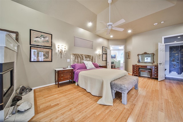 bedroom with lofted ceiling, a tile fireplace, ensuite bathroom, light hardwood / wood-style flooring, and ceiling fan