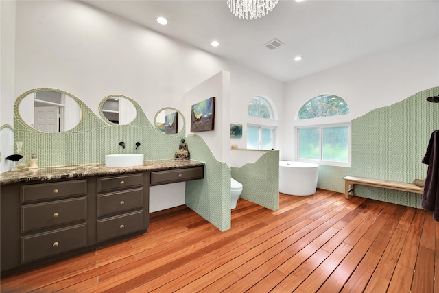 bathroom with an inviting chandelier, a tub to relax in, toilet, vanity, and hardwood / wood-style flooring