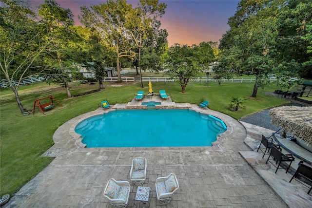 pool at dusk featuring a patio and a lawn