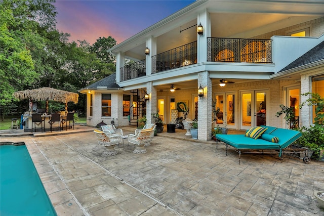 back house at dusk featuring ceiling fan, a balcony, and a patio