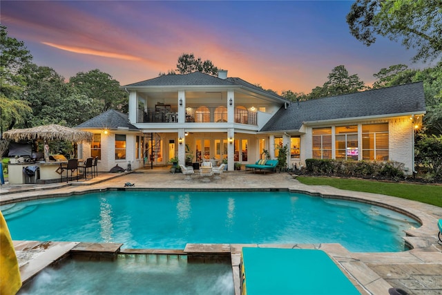 back house at dusk featuring a patio area, a balcony, an outdoor bar, and exterior kitchen