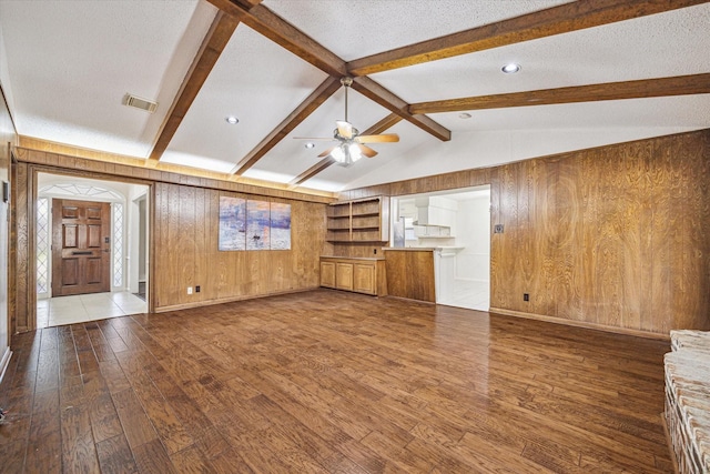 unfurnished living room with a textured ceiling, ceiling fan, wooden walls, wood-type flooring, and vaulted ceiling with beams