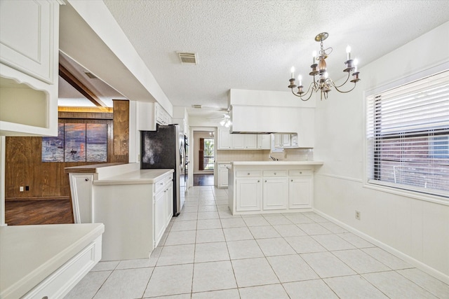 kitchen featuring pendant lighting, an inviting chandelier, white cabinets, kitchen peninsula, and stainless steel refrigerator