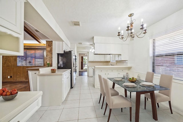 kitchen with white cabinetry, a notable chandelier, stainless steel fridge, pendant lighting, and light tile patterned floors