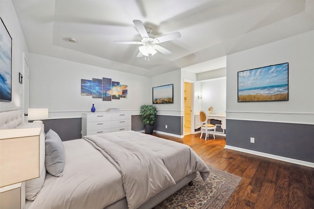 bedroom with dark hardwood / wood-style floors, ceiling fan, and a tray ceiling