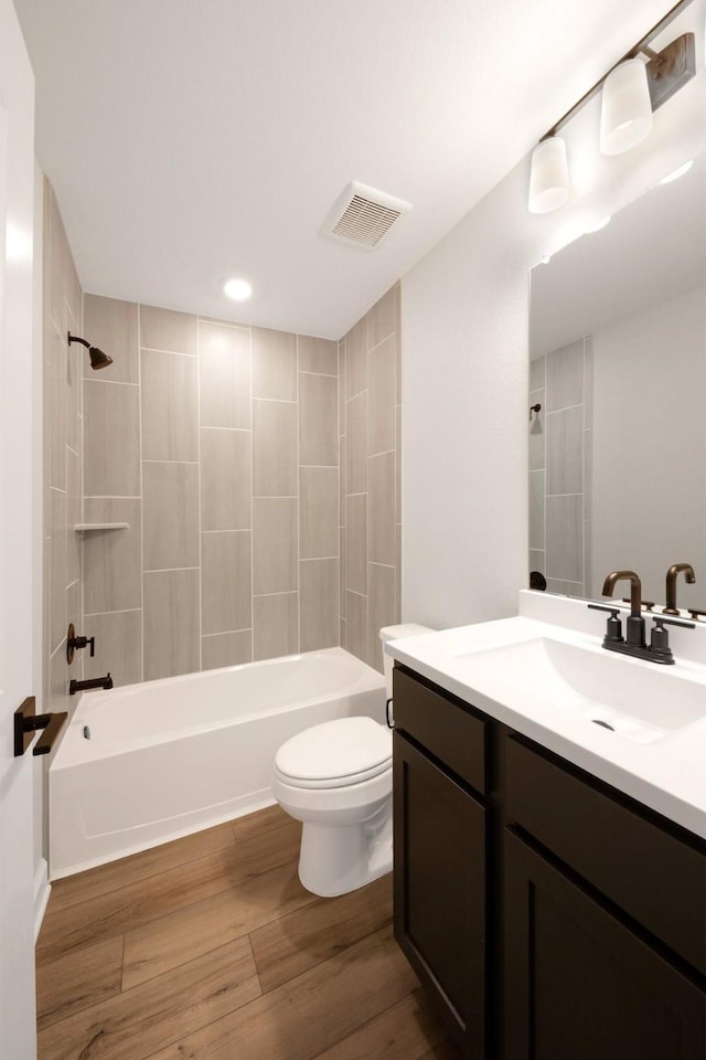 full bathroom with hardwood / wood-style floors, tiled shower / bath combo, toilet, and vanity