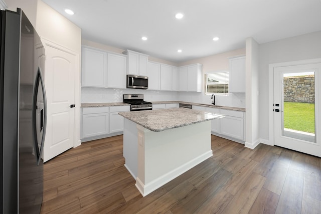 kitchen with white cabinetry, light stone counters, dark hardwood / wood-style floors, a kitchen island, and appliances with stainless steel finishes