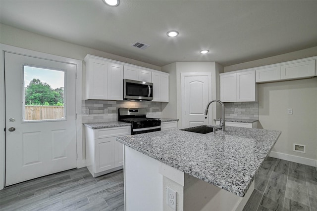 kitchen featuring white cabinets, sink, appliances with stainless steel finishes, and an island with sink