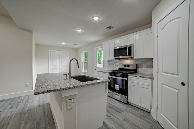 kitchen with white cabinets, a center island with sink, sink, appliances with stainless steel finishes, and light stone counters