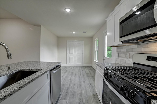 kitchen with appliances with stainless steel finishes, light stone counters, white cabinetry, and sink