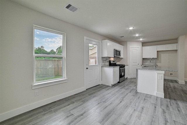 kitchen featuring a center island with sink, white cabinets, decorative backsplash, appliances with stainless steel finishes, and light stone counters