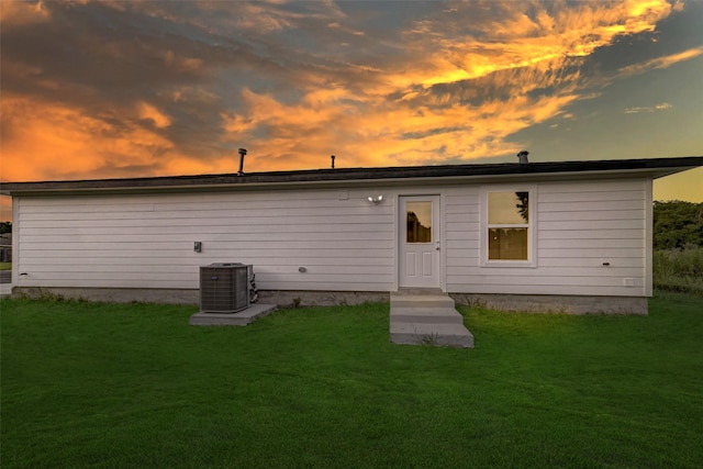 back house at dusk featuring central air condition unit and a yard