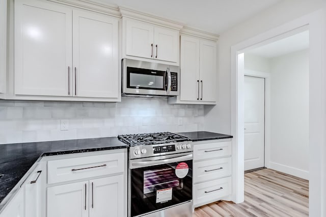 kitchen with tasteful backsplash, white cabinets, dark stone counters, and appliances with stainless steel finishes