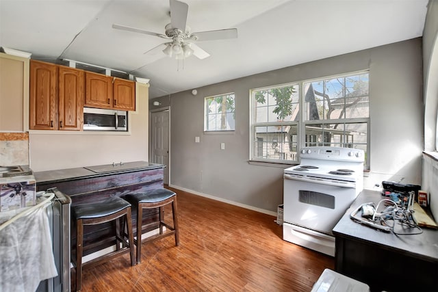 kitchen featuring brown cabinets, white electric range, stainless steel microwave, wood finished floors, and ceiling fan